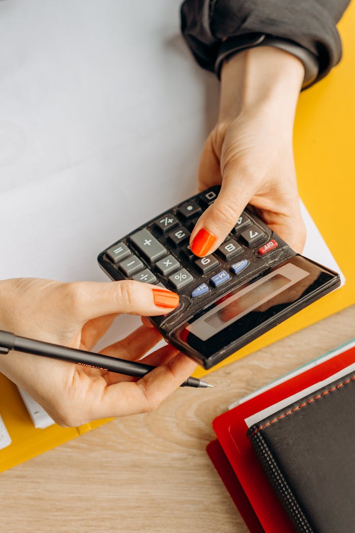Hands using a calculator on a desk surrounded by stationery, embodying business and finance themes.
