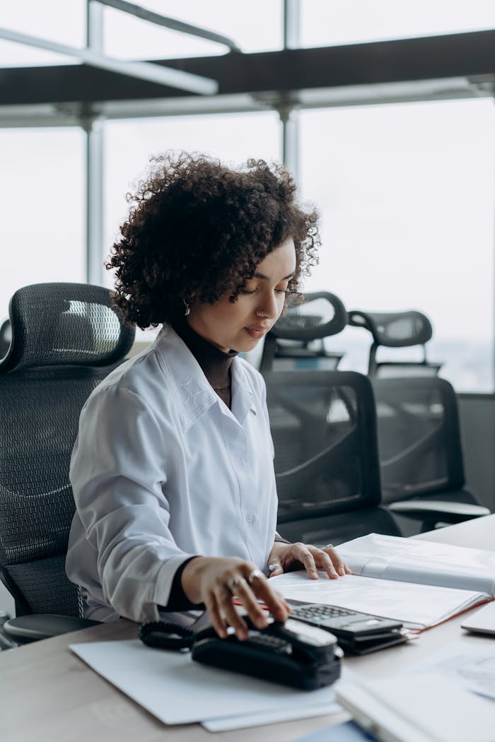 Young woman with curly hair working at a modern office desk, calculating numbers with focus.